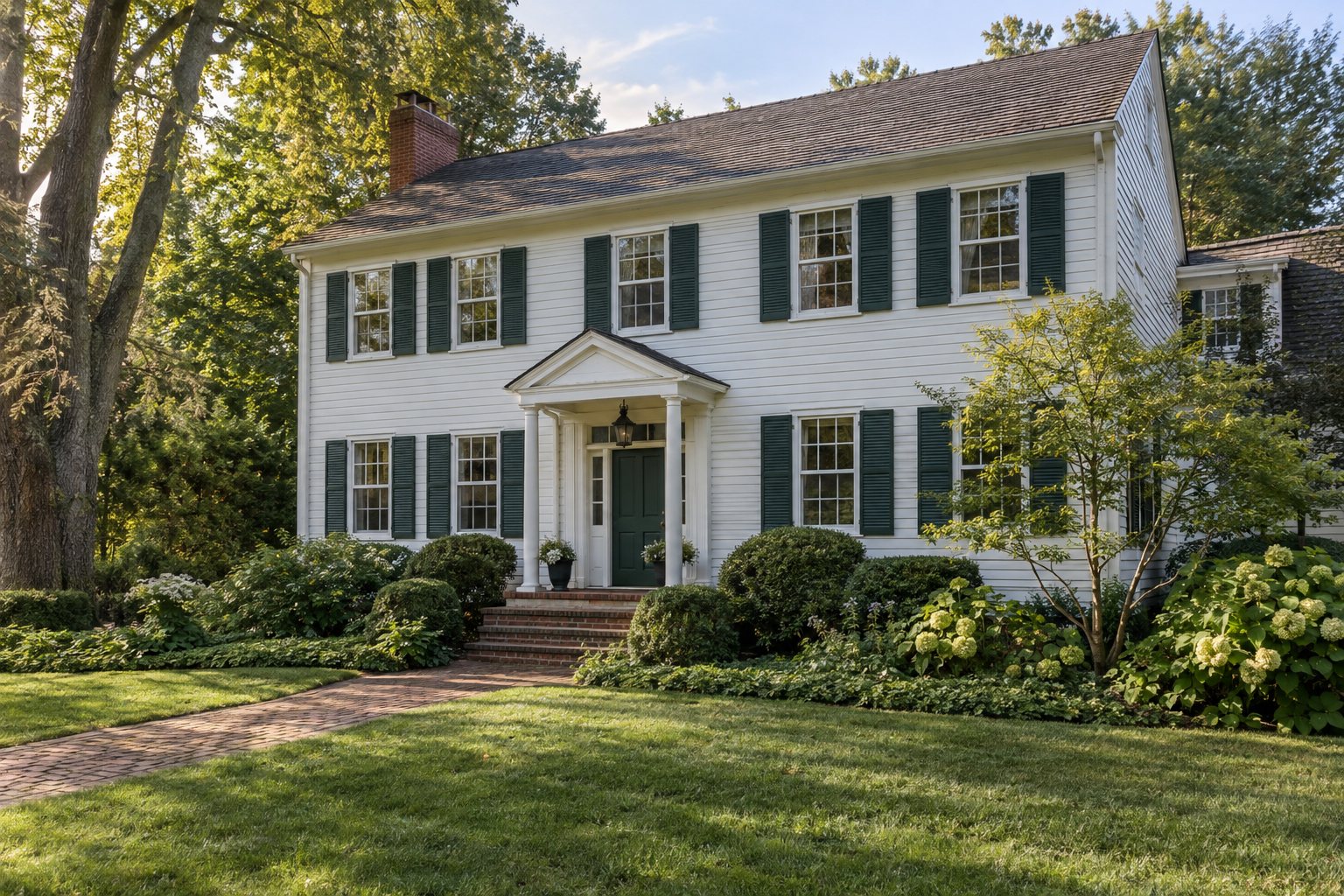 White clapboard home with dark louvered shutters, a welcoming front entry, and landscaped garden