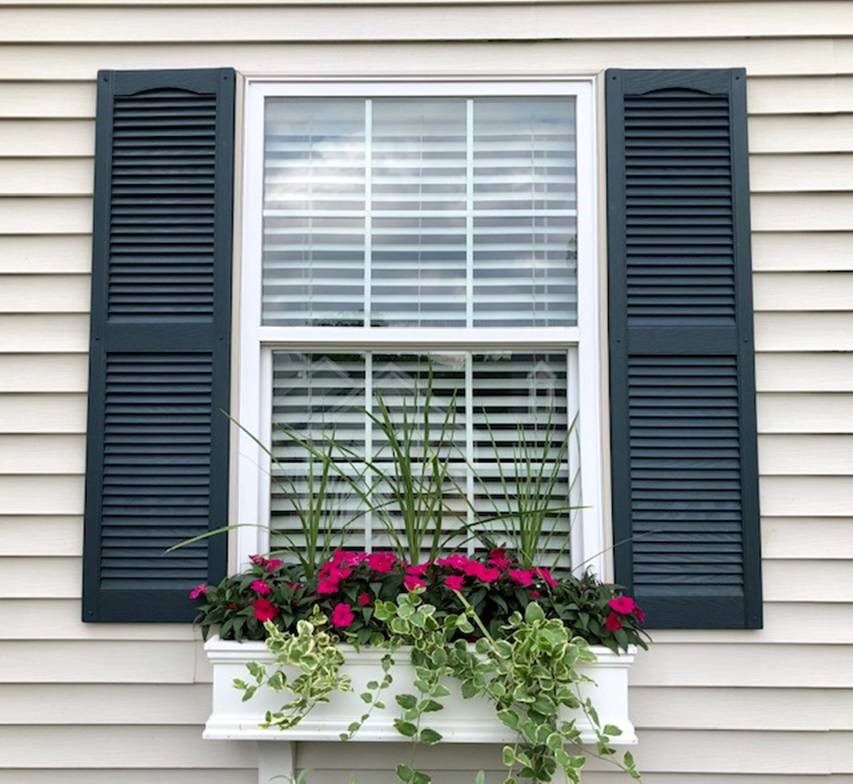 Black louvered shutters installed beside a house window
